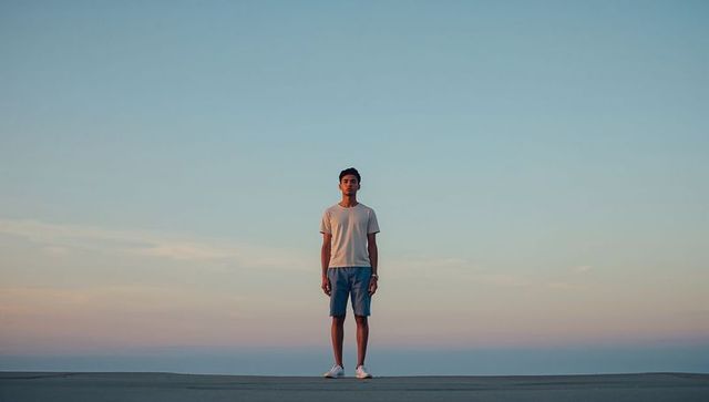 Young man standing on wide open horizon under pastel dusk sky for minimal lifestyle