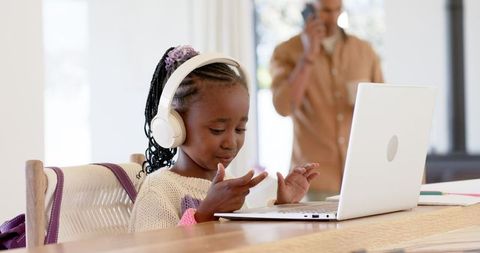 African american girl wearing headphones using laptop for remote learning and family life