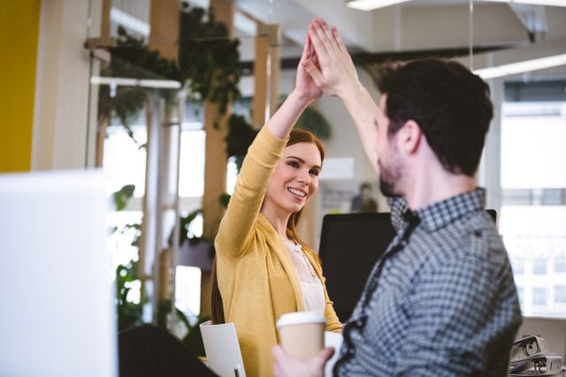 Happy businesswoman giving high-five to male coworker in creative office