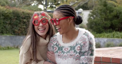Friends laughing together wearing red novelty glasses in cozy sweaters outdoors