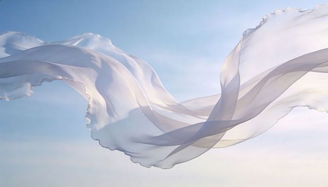 Ethereal white chiffon billowing across soft blue sky with sunlit transparency