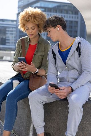 Young couple sitting and sharing smartphones on urban plaza, casual city lifestyle daylight