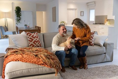 Middle-aged couple relaxing on cozy modern sofa petting dog in warm neutral living room