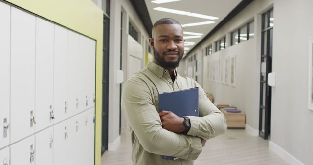 Young man confidently standing in a modern hallway with a folder, ideal for educational materials, college brochures, and professional growth concepts.
