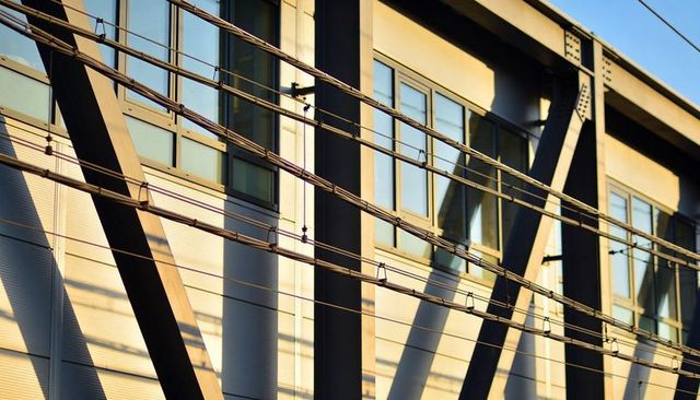 Tramway wires and steel bracing crossing modern glass facade at golden hour urban architecture