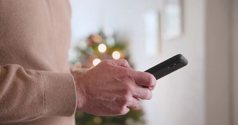 Man using smartphone near christmas tree in cozy living room