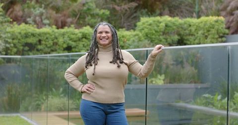 Mature african american woman standing by pool smiling while resting hand on glass railing