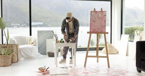 Indian artist painting in bright lakeside studio, minimalist space with easel and canvases