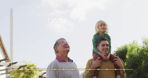Grandfather gazing skyward while father carries son on shoulders in sunlit backyard