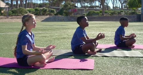 Children practicing outdoor mindfulness yoga on mats at school field for wellness