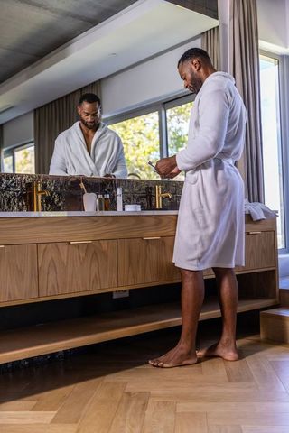 African american man grooming at modern bathroom vanity in white robe