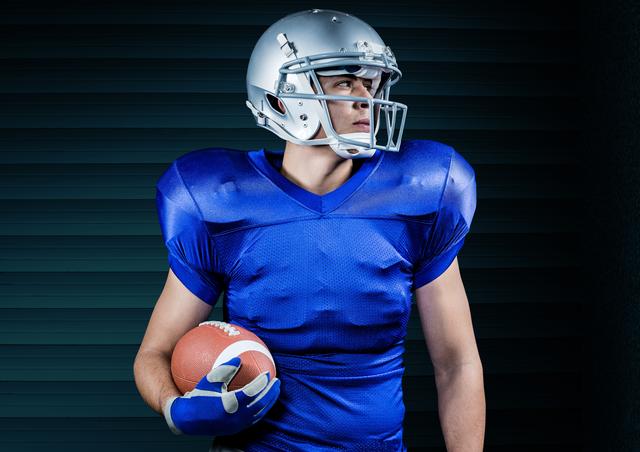 American football player in blue jersey holding a football while looking to the side. Ideal for sports-related content, advertisements for sports equipment, team promotions, or athletic training publications.