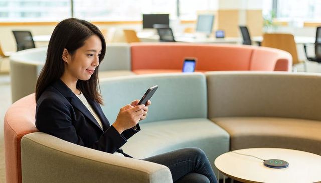 Asian businesswoman using smartphone on curved office sofa in modern coworking lounge