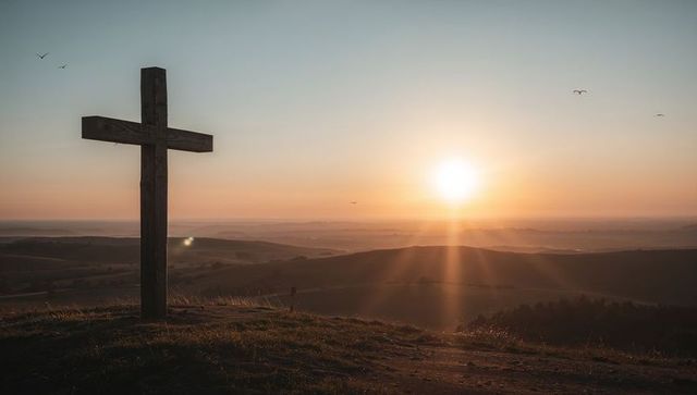 Wooden Cross Standing on Hill at Golden Sunrise Casting Long Rays over Valley Landscape