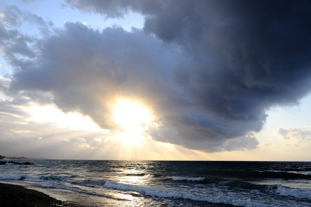 Dynamic sunrise with dark storm clouds over the ocean waves. Ideal for use in travel blogs, weather forecasts, nature-inspired art projects, and backgrounds emphasizing both serenity and power of nature.