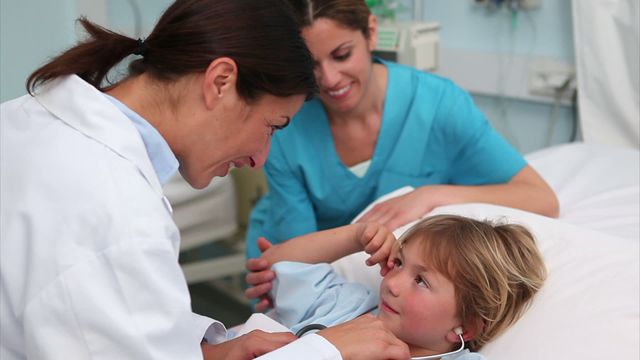 A doctor is using a stethoscope to examine a young boy in a hospital room, while a nurse stands by with a warm smile. This scene conveys empathy and professional medical care. Suitable for advertising medical services, pediatric healthcare promotions, or educational materials on patient care and child health.