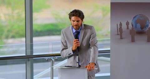 depicts a business professional in suit engaging the audience at a seminar. the expressive speaker is standing at a podium with microphone, symbolizing corporate communication and public speaking. ideal for marketing materials or publications related to business events, conferences, or communication training.