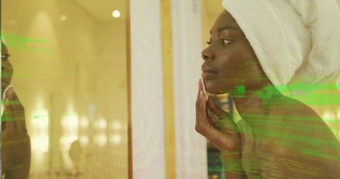 African American Woman Applying Skincare with Cotton Pad at Mirror Wearing White Towel