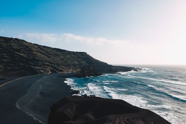 This breathtaking scene captures a black sand beach with rugged rocky cliffs bordering a vibrant blue ocean. Perfect for use in travel articles, blogs, environmental publications, and as background imagery for websites promoting beach destinations and outdoor activities.