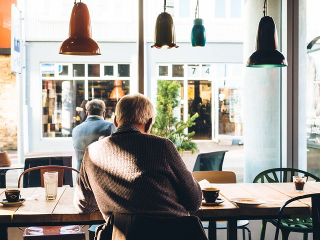 Elderly man sits alone in a modern café, enjoying a moment of solitude. Ideal usage includes themes of aging, contemplation, relaxing environments, and solo activities.