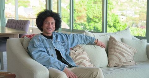 Relaxed african american man sitting on sofa in sunlit open-plan living room with green view