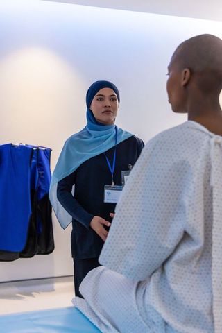 Clinician wearing blue hijab consulting patient on exam table in bright modern clinic