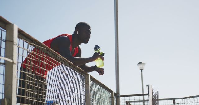 African american man drinking from water bottle and taking break in exercise outdoors. fitness, healthy and active lifestyle concept.