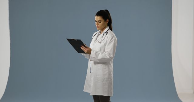 The female doctor is reviewing medical records with focus while standing in a clinical setting. Her attentive posture implies preparation for a patient consultation or in-depth study. This can be used for medical blogs, healthcare services promotions, or educational materials highlighting medical professionalism.