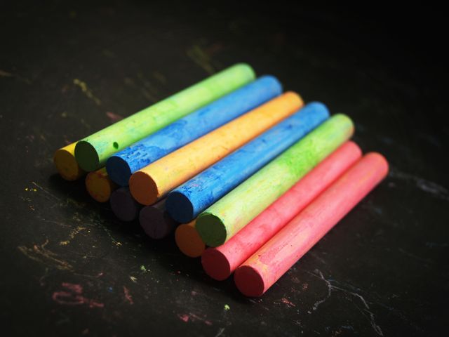 Colorful chalks neatly arranged on a blackboard. Perfect for designs related to education, creativity, schools, and teaching aids. Great for illustrating ideas around children's learning and artistic activities.