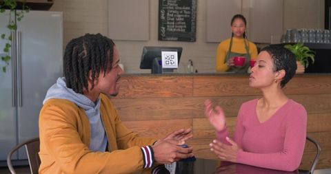 Young couple having animated conversation in cozy coffee shop with barista in background