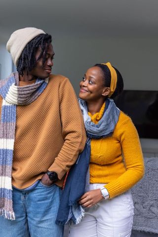 African american couple wearing knit scarves and sweaters sharing warm smiles at home