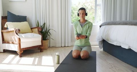 Woman Practicing Yoga in Bedroom with Smart Device and Headphones