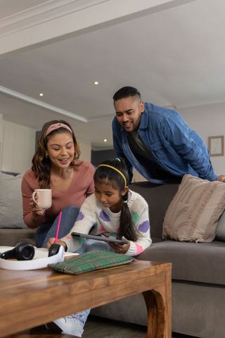 Parents helping daughter with homework on tablet in cozy living room — family learning moment