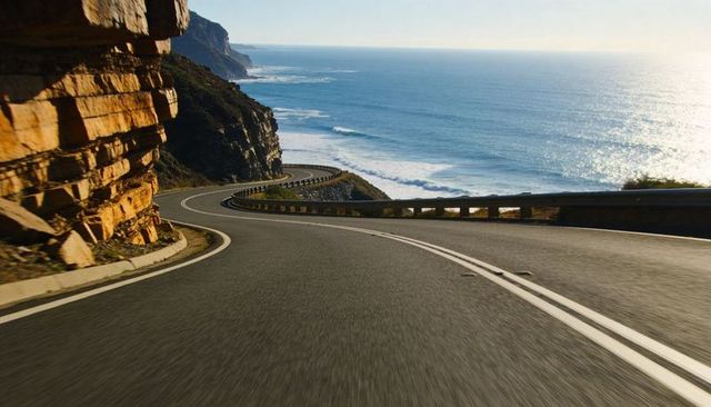 Sunlit coastal road curving along sandstone cliffs overlooking sparkling ocean