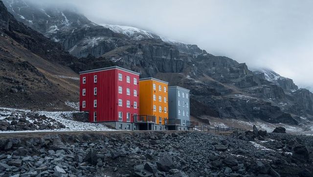 Bright red, yellow, blue coastal cabins on stilts by rocky shore beneath foggy cliffs