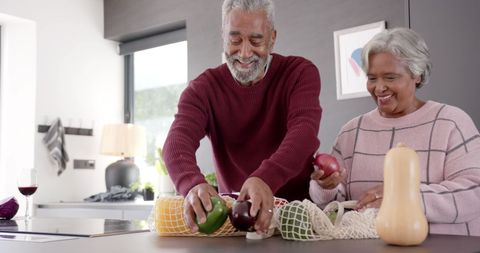 Joyful senior couple unpacking groceries in modern kitchen