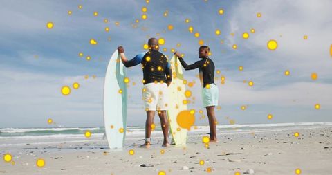 Two men holding surfboards on sunny beach with orange dot overlay suggesting wellness
