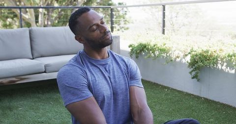 Man stretching torso on sunny balcony turf during outdoor morning fitness and recovery
