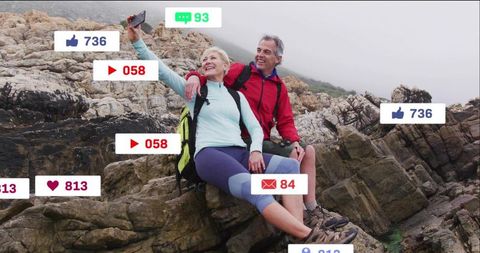 Mature couple posing on coastal rocks taking selfie with social media reaction overlays
