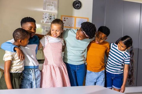 Diverse elementary students linking arms and smiling together in bright classroom