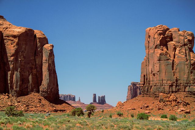 Stunning view of Monuments Valley with majestic red rock formations standing tall under a clear blue sky. Perfect for use in travel promotions, nature-themed websites, educational materials, and desktop wallpapers. Ideal to showcase the beauty of natural landscapes and iconic geological formations.