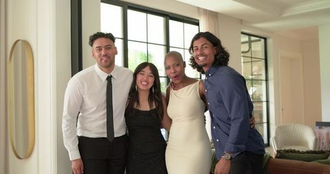 Multiracial friends posing in modern living room wearing formal outfits and smiling at event