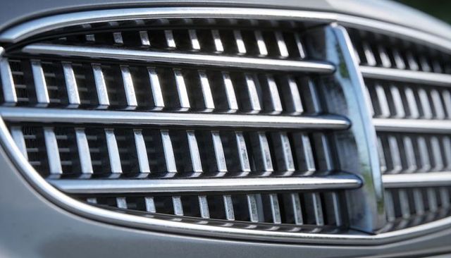 Macro chrome car grille showing central slats, surface scratches and green reflections
