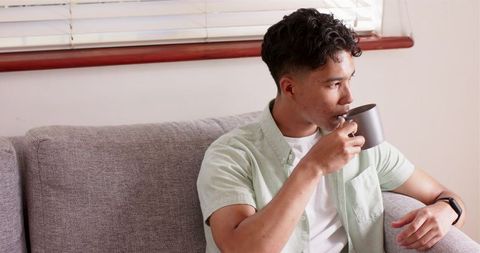 Man Drinking Coffee on Couch Reflecting in Morning Light