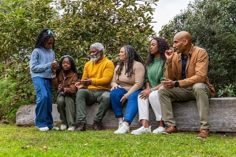 Multigenerational african american family sharing smartphone on log bench in park outdoors