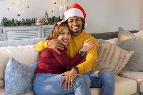 Couple hugging on couch wearing santa hat and cozy sweaters celebrating holiday joy