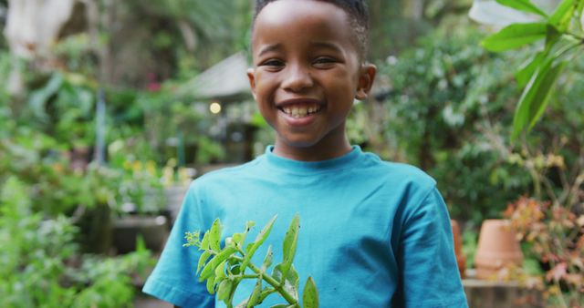 Portrait of happy african american boy holding plant in garden. Spending time outdoors, working in garden nursery.