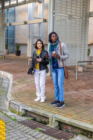 Diverse young professionals standing on urban plaza holding coffee cups and smartphones