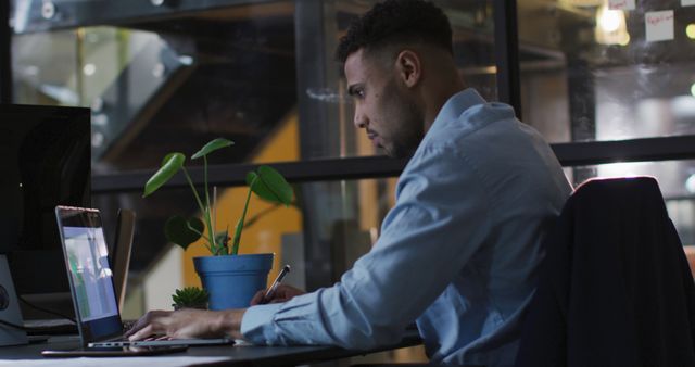 Young professional man working late night in modern office. Could be used for business, productivity, technology, modern work environments, and corporate topics.