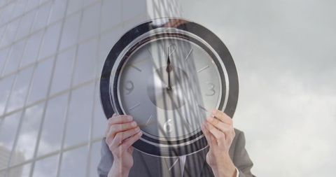 Businessman holding clock hiding face against glass skyscraper reflection